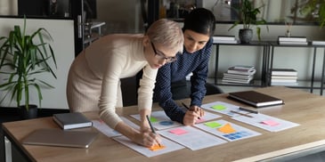 Conheça os conceitos de produto e de projeto. Descrição da imagem: duas mulheres profissionais de marketing fazendo um planejamento.