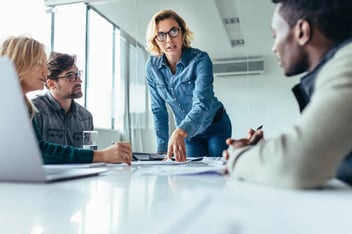 Conheça o modelo de gestão Management 3.0. Descrição da imagem: gestora passando orientações para a equipe em sala de reuniões.