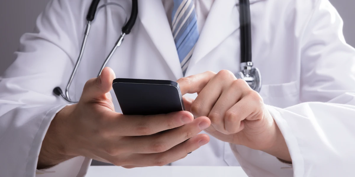 Detalhe das mãos de um médico usando o celular. Conceito de uso ético das redes sociais pelos profissionais de saúde.