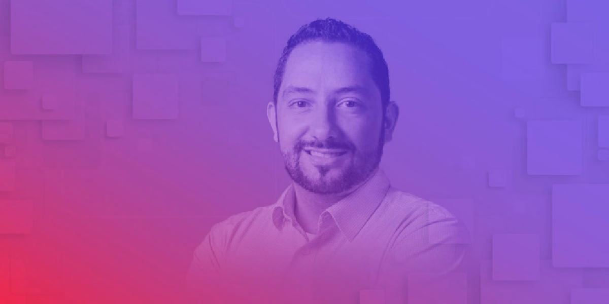 Um homem com barba está sorrindo em frente a um fundo roxo e vermelho.
